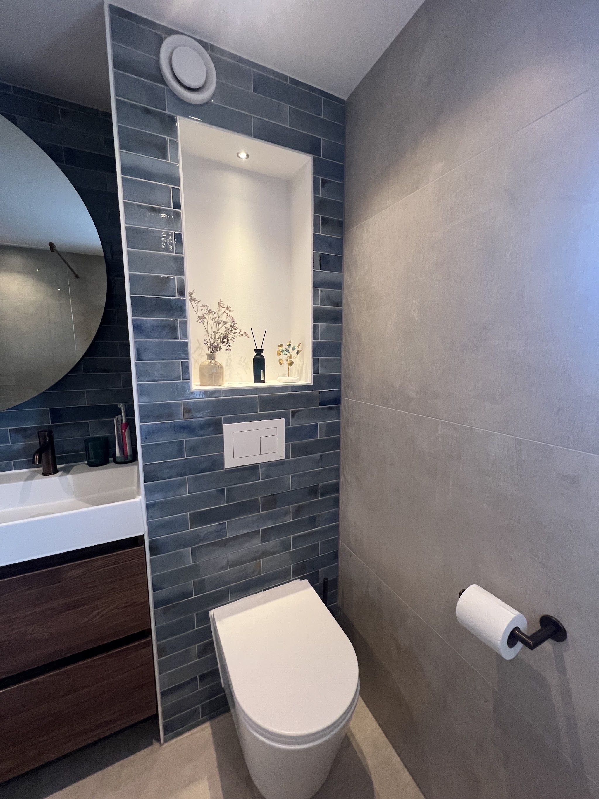 Toilet met blauwe staande tegels, verlichte nis en badmeubel met donkere lades