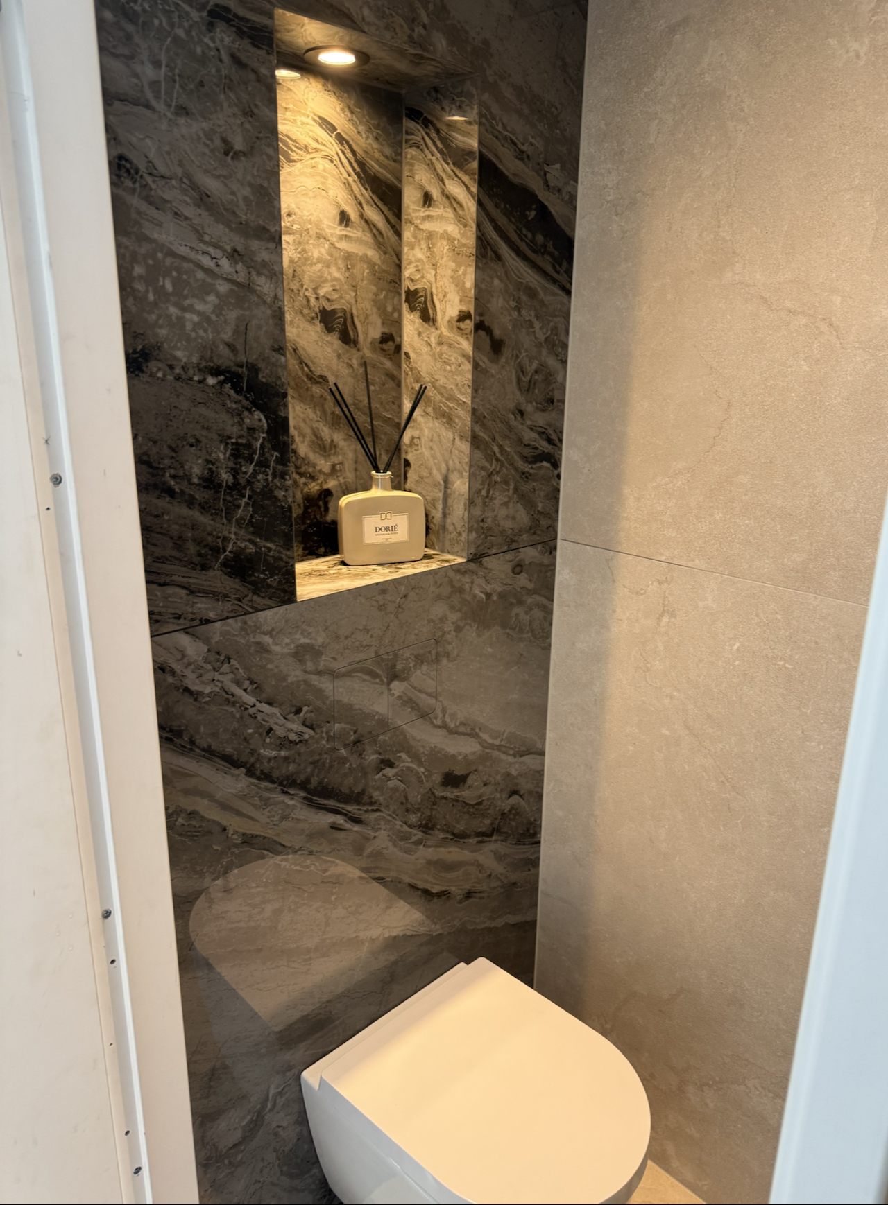 Hangtoilet onder een verlichte nis, wand in donker marmerdessin naast lichte grootformaat tegels