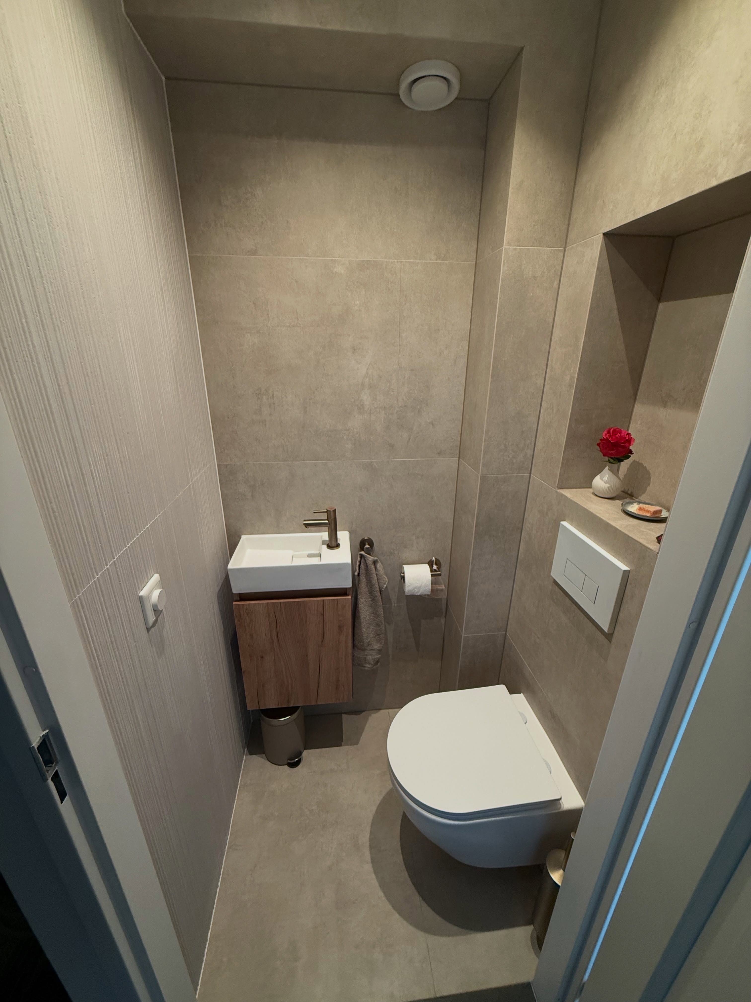 Compact toilet met lichte grootformaat tegels, fonteintje op houten kastje en een nis in de wand