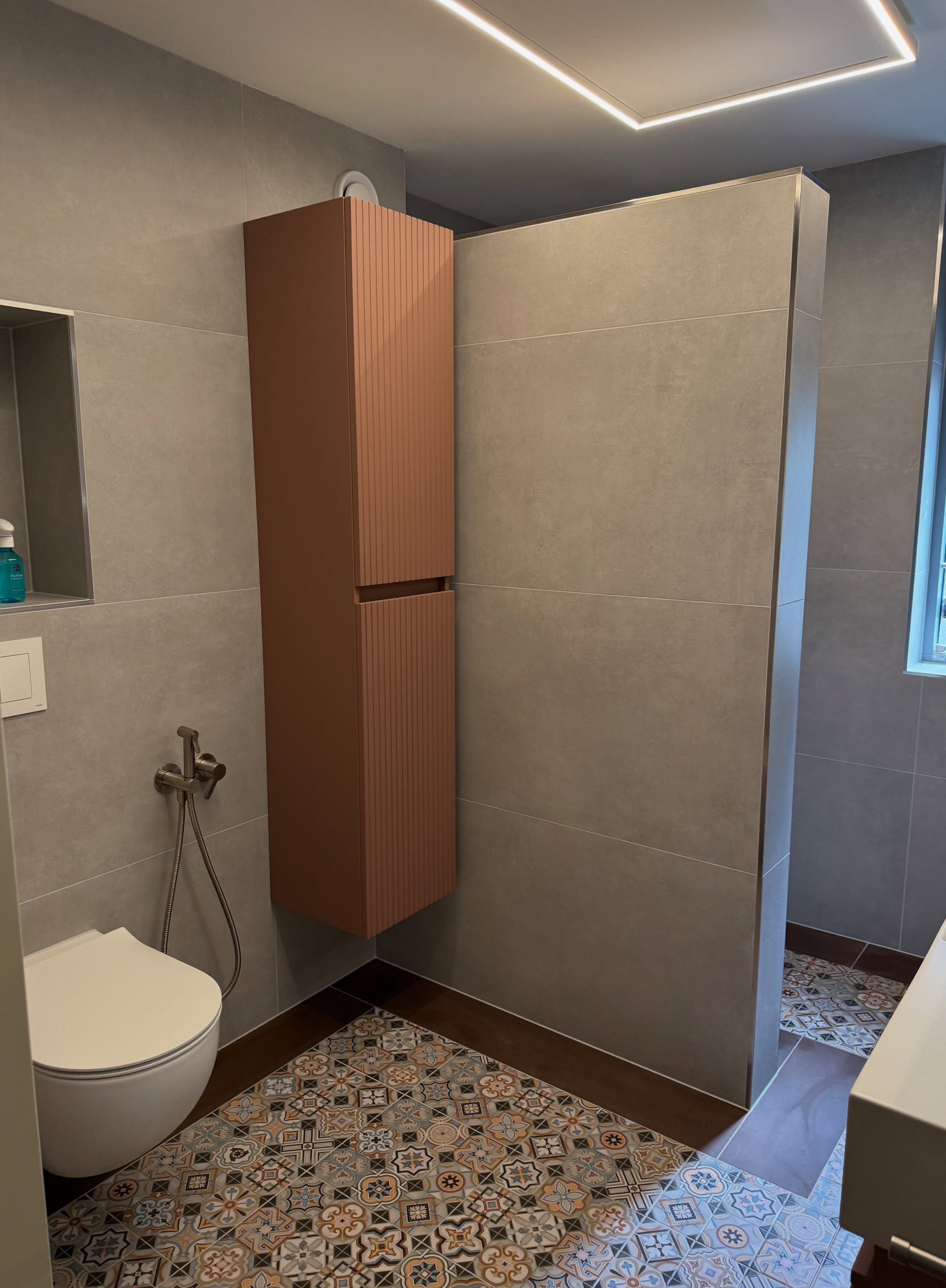 Gerenoveerde badkamer met tegelvloer met patroon, terracotta hoge kast en hangtoilet